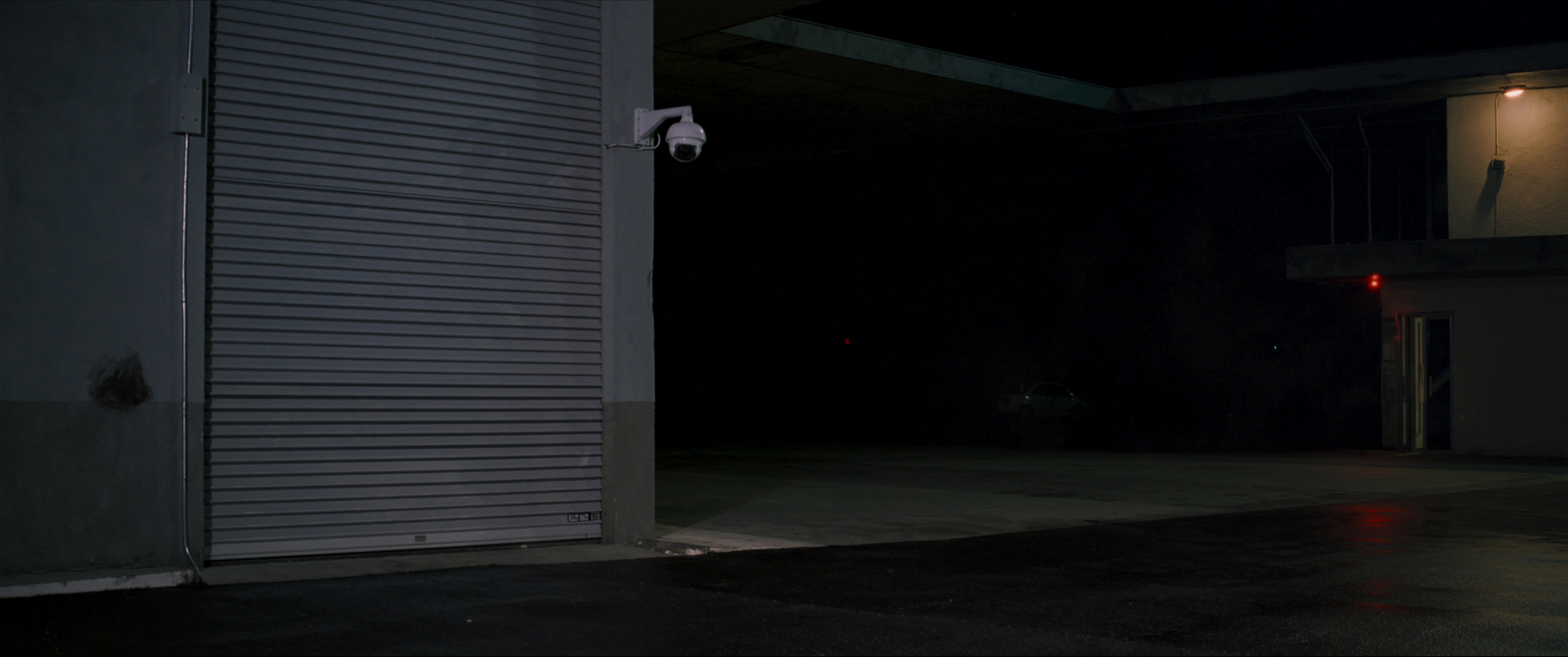 A small commercial unit at night with the shutter down and a security camera on the corner