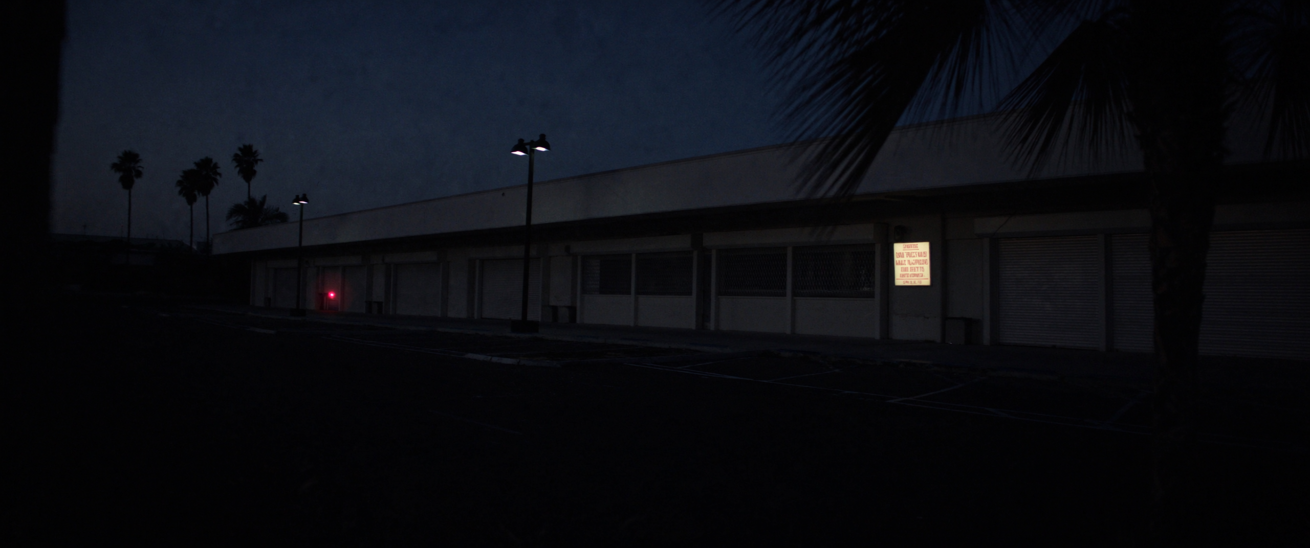 A multi-tenant commercial plaza at dusk with an empty parking lot