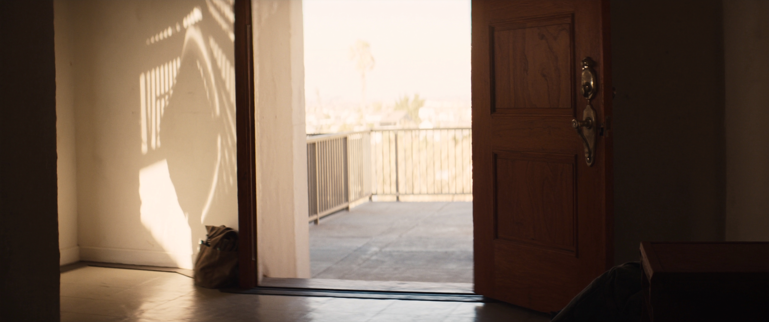 The entry hall of a home in warm daylight with the front door open and a tool bag set down inside